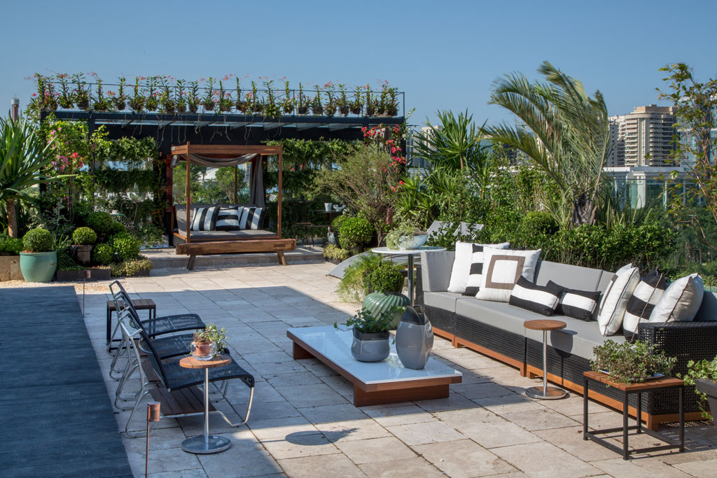 CASACOR Rio de Janeiro 2014. Anna Luíza Rothier desenhou um jardim simétrico com três grandes espelhos d'água, cercados de verde no espaço Rooftop Garden. Muitas palmeiras tomam conta das jardineiras. Os bouganvilles cobrem o gazebo. Plantas rasteiras, através do vidro do guarda-corpo, se confundem com a paisagem de fora. O piso é travertino, da Hardscape. Os móveis externos, dos estofados às mesas, são da MAC e totalmente à prova d'água.