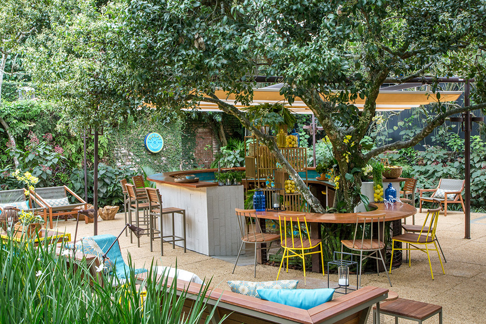 CASACOR Rio de Janeiro 2016. Bar de Gin - Fernanda Sampaio, Júlia Sampaio e Raísa Rodrigues. As profissionais destacam a sustentabilidade no projeto, que aproveita o potencial de materiais naturais como pedra e madeira. Na base em tons arenosos e neutros, elas pincelam toques de azul e amarelo no mobiliário em madeira, alumínio e fibras sintéticas.