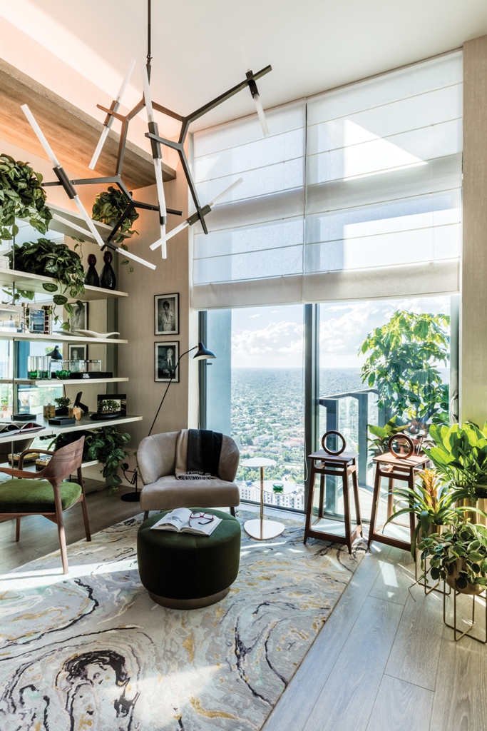 CASACOR Miami. Multi-Use Space for the Modern Man - Tatiana Moreira. O quarto funciona como biblioteca, home office, living, bar e quarto de hóspede com cama retrátil em apenas 27 m², para um homem da metrópole que não abre mão da luz do sol. Cinza claro, verde militar, rosa pálido e ouro afirmam o mood urbano do projeto. Sobre o piso de nogueira, um tapete claro abstrato que parece mármore.