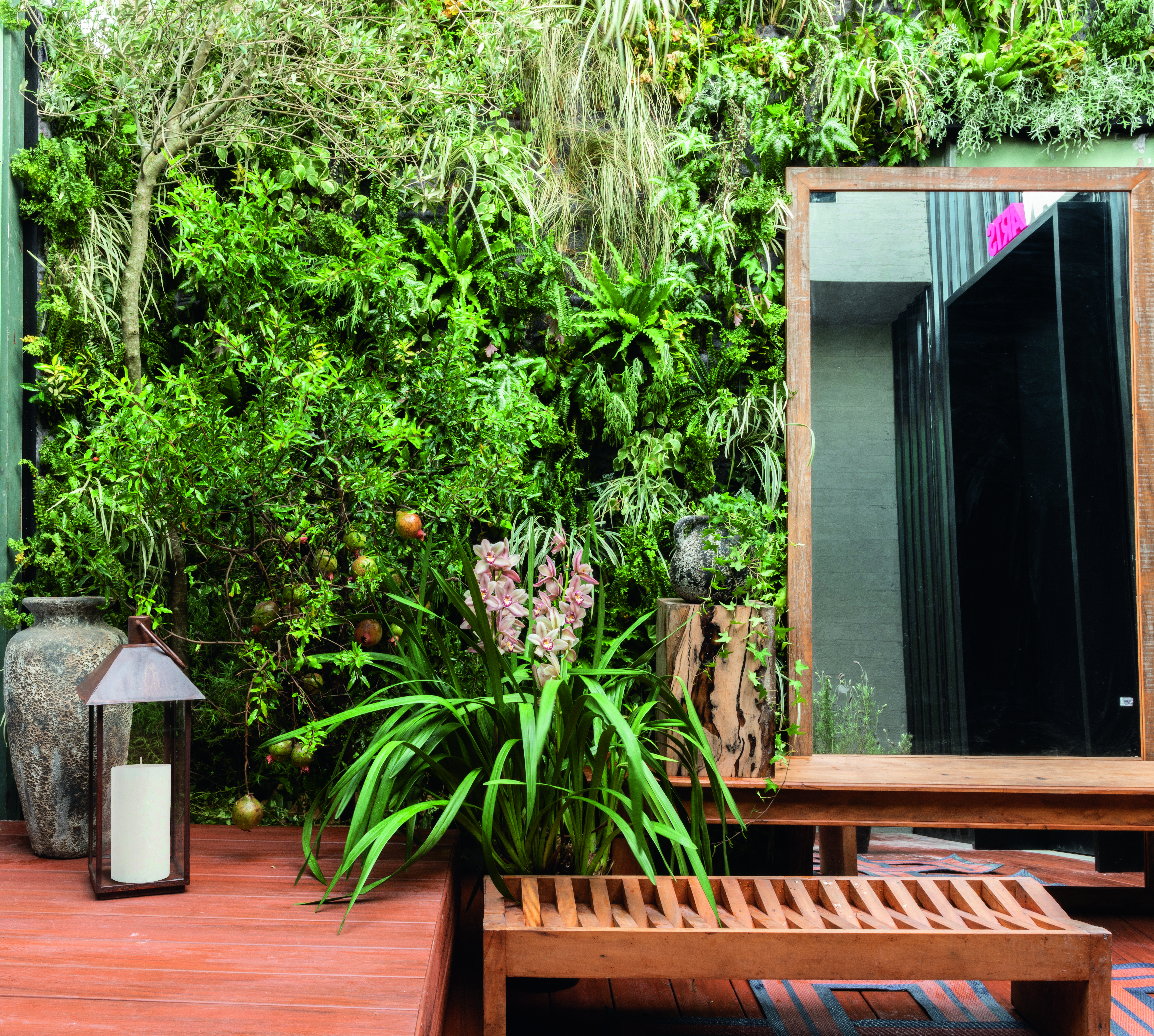 CASACOR São Paulo 2018. Jardim do Entardecer - Myrian Marquez. Oliveiras e romãzeiras em vasos, entre outras plantas, criam uma atmosfera onírica que celebra o feminino. Mais precisamente, as ninfas gregas Hespérides, que personificam o entardecer. O banco de madeira ecológica convida a apreciar a paisagem.