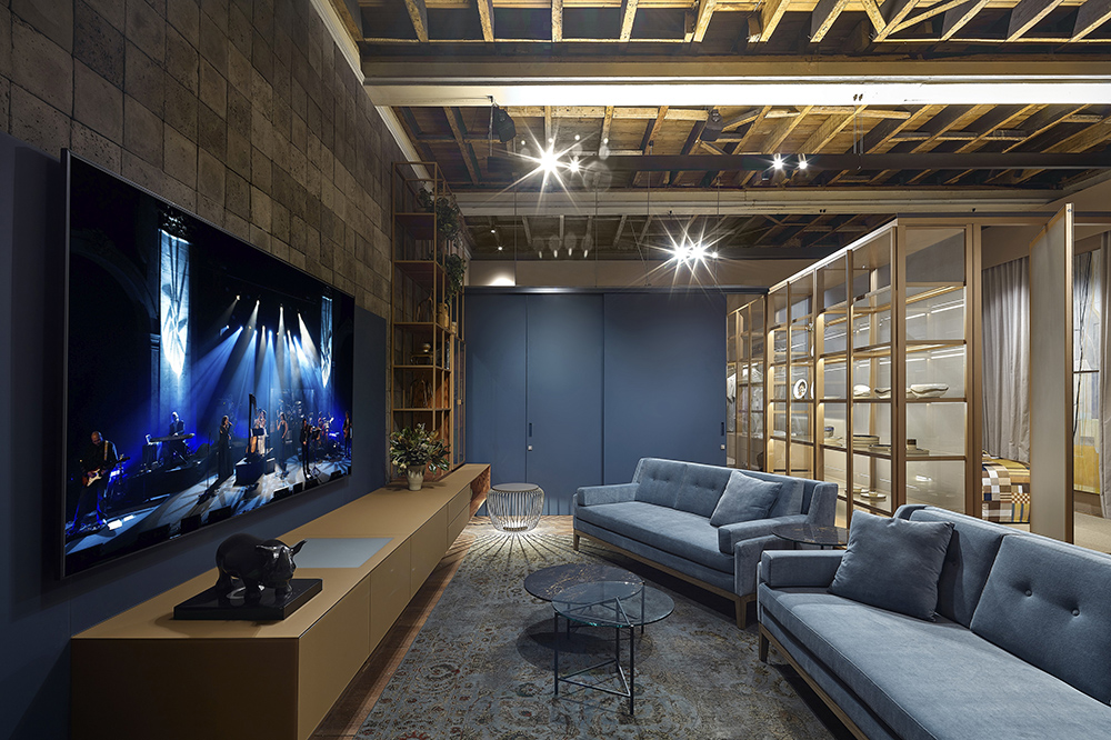 Studio Sumisura - Gislene Lopes. A parede ao fundo do ambiente o os sofás na cor azul são os destaques do ambiente, integrado por painéis pivotantes de vidro que integram os ambientes sem roubar a cena