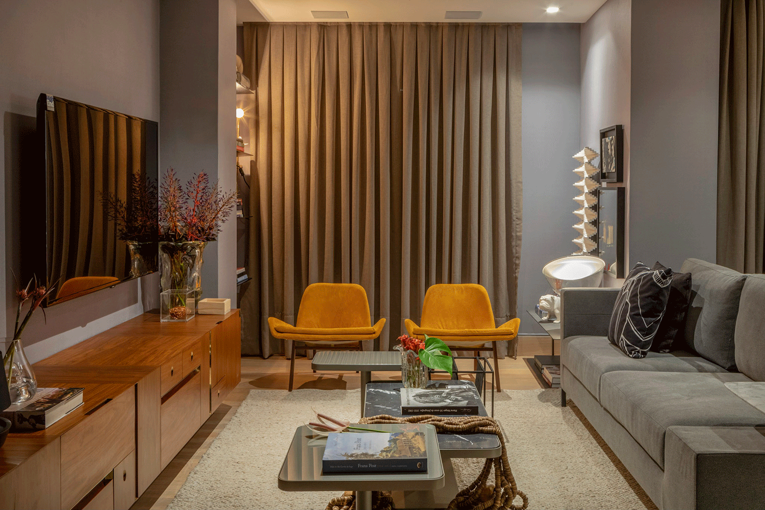 Studio Premium - Fábio Bouillet e Rodrigo Jorge. A décor assume tons de cinza e preto, sem perder a descontração carioca e celebrando o design brasileiro. A madeira do aparador vem num tom quente, acompanhando o mostarda das cadeiras. No geral, os contrastes não são marcados, criando uma composição sóbria e acolhedora.