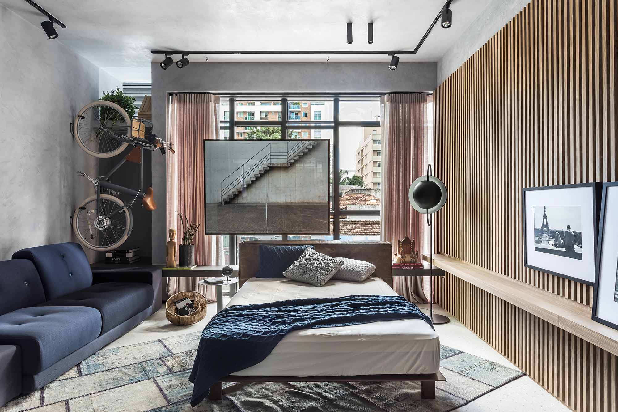 CASACOR Paraná: Studio 33 - Carla Grudtner. O estilo de vida de um jovem fotógrafo especializado em arquitetura e interiores foi o ponto de partida neste espaço de 36 m². Uma das sacadas para trazer amplitude foi abusar da luz, que entra pelas grandes aberturas. Nas paredes, textura de cimento queimado, madeira ripada e porcelanato que lembra graniste no piso. A bike, meio de transporte do fotógrafo, ganha lugar de destaque, assim como os registros emoldurados.