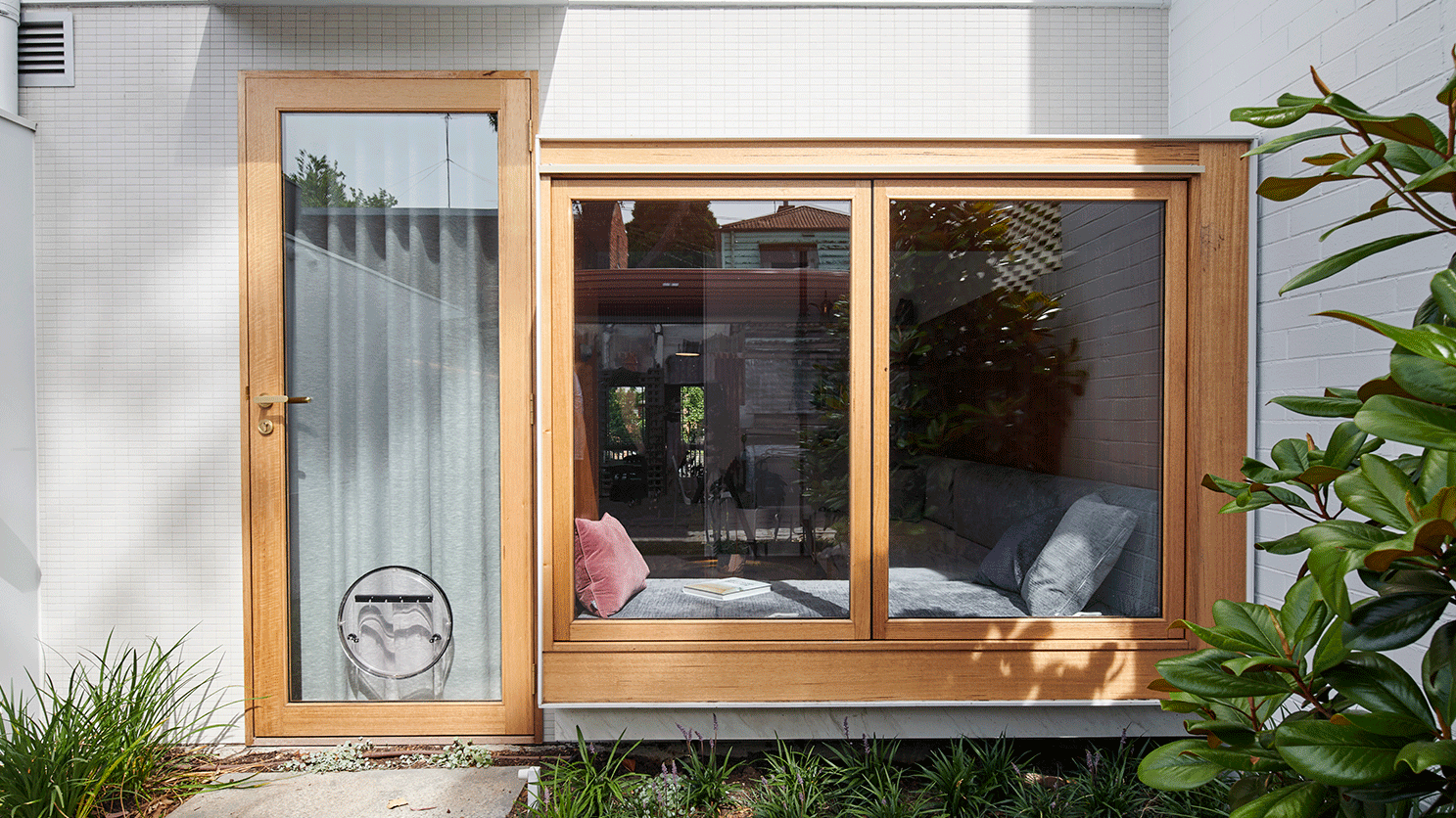 Porta para o quinta vista de fora, um gif com as janelas de vidro e moldura de madeira abrindo. À esquerda, a porta de vidro com moldura em madeira e uma porta redonda para cachorro coberta com uma cortina interna.