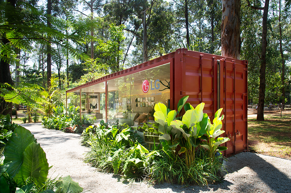 Contêiner vermelho visto do lado de fora, envolto por jardim, com logo da LG aparente.