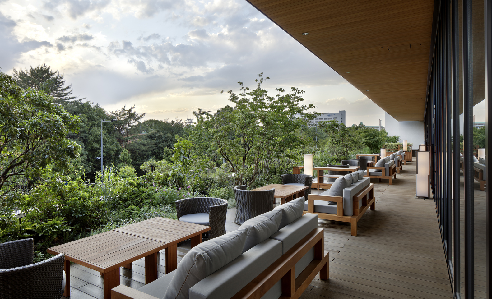 Deck com sofás mesas e poltronas com vista para exuberante área verde do parque