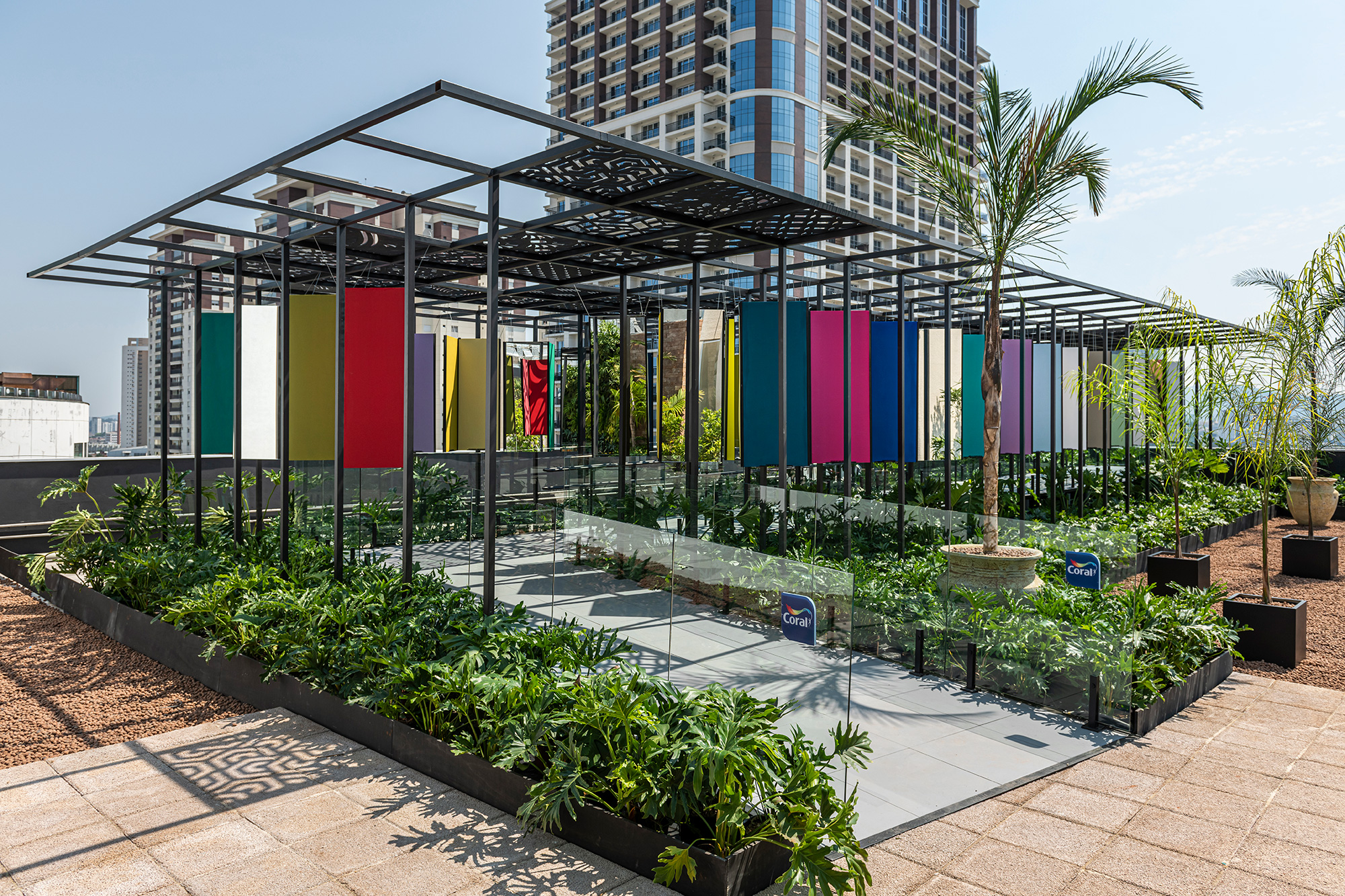 Fernando Brandão - "ESPAÇO CORAL Uma janela para o amanhã". Ocupando uma área de 200m² no rooftop da mostra, o arquiteto desenvolveu um espaço de contemplação para o lançamento da nova paleta de cores da Coral Colour Future 2022. Uma passarela conduz os visitantes a uma galeria de atmosfera lúdica envolvida por vegetação e totem coloridos suspensos que foram dispostos em ambos os lados. Na cobertura, treliças trabalhadas filtram o sol e criam efeitos interessantes de sombras no chão. O paisagismo por Mônica Costa e a luminotécnica, Guinter Parschaski.