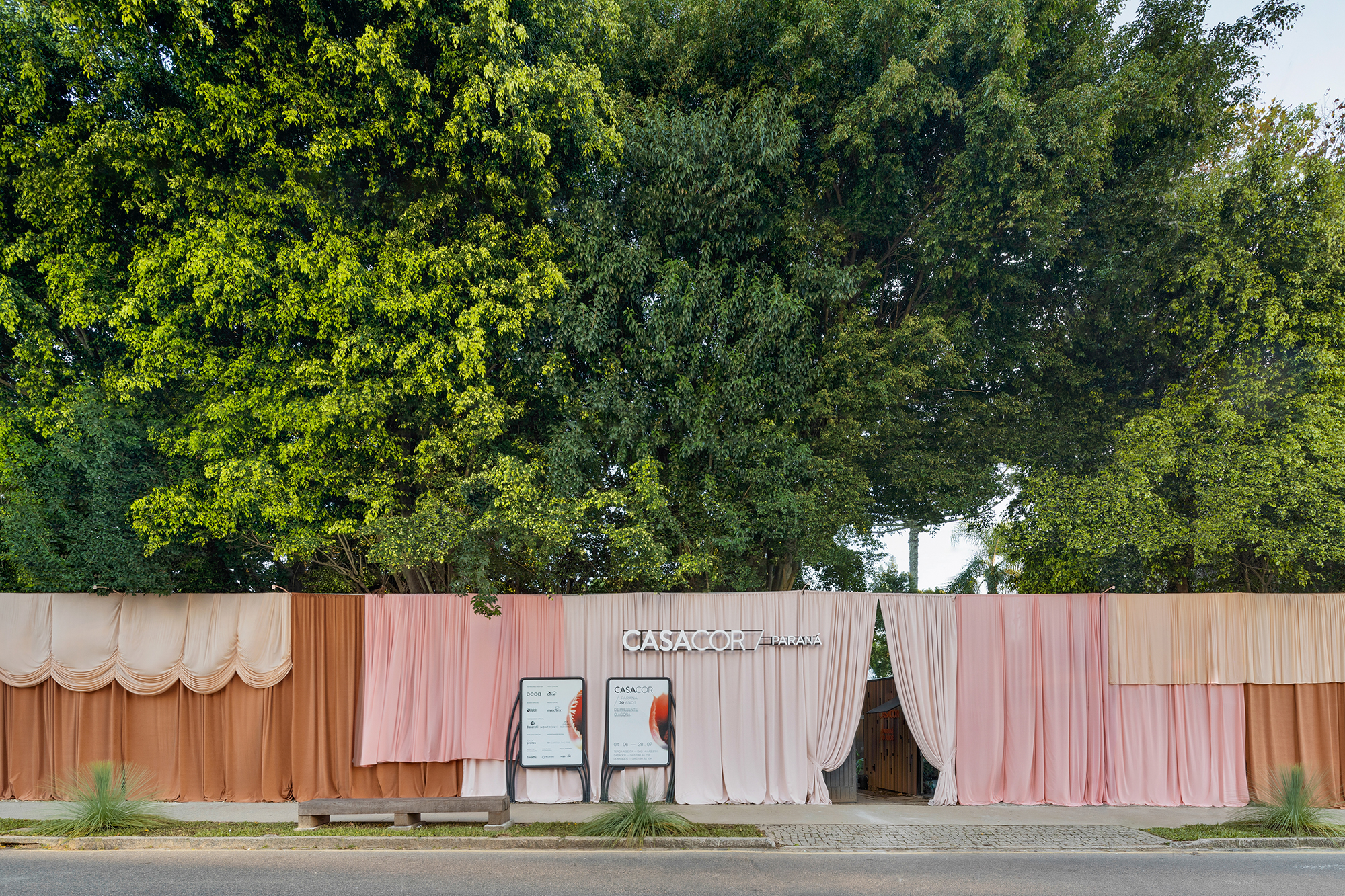 <b>Nicholas Oher e Paloma Bresolin - Fachada. </b>A fachada da CASACOR Paraná é mais do que a face principal do casarão que sedia a mostra, é a promessa de uma experiência visual envolvente. O tema deste ano inspira os profissionais a oferecer um presente arquitetônico para Curitiba, transcendendo a norma de maneira inédita. A partir deste conceito, a construção é embrulhada com uma cortina de 30 metros de largura, que mescla diferentes texturas, volumes e tamanhos. A paleta cromática contempla tons de goiaba, pêssego, caju e rosa, todos conectados com sensações positivas. Toda a composição visa incentivar o cuidado com a beleza da vida que nos circunda.