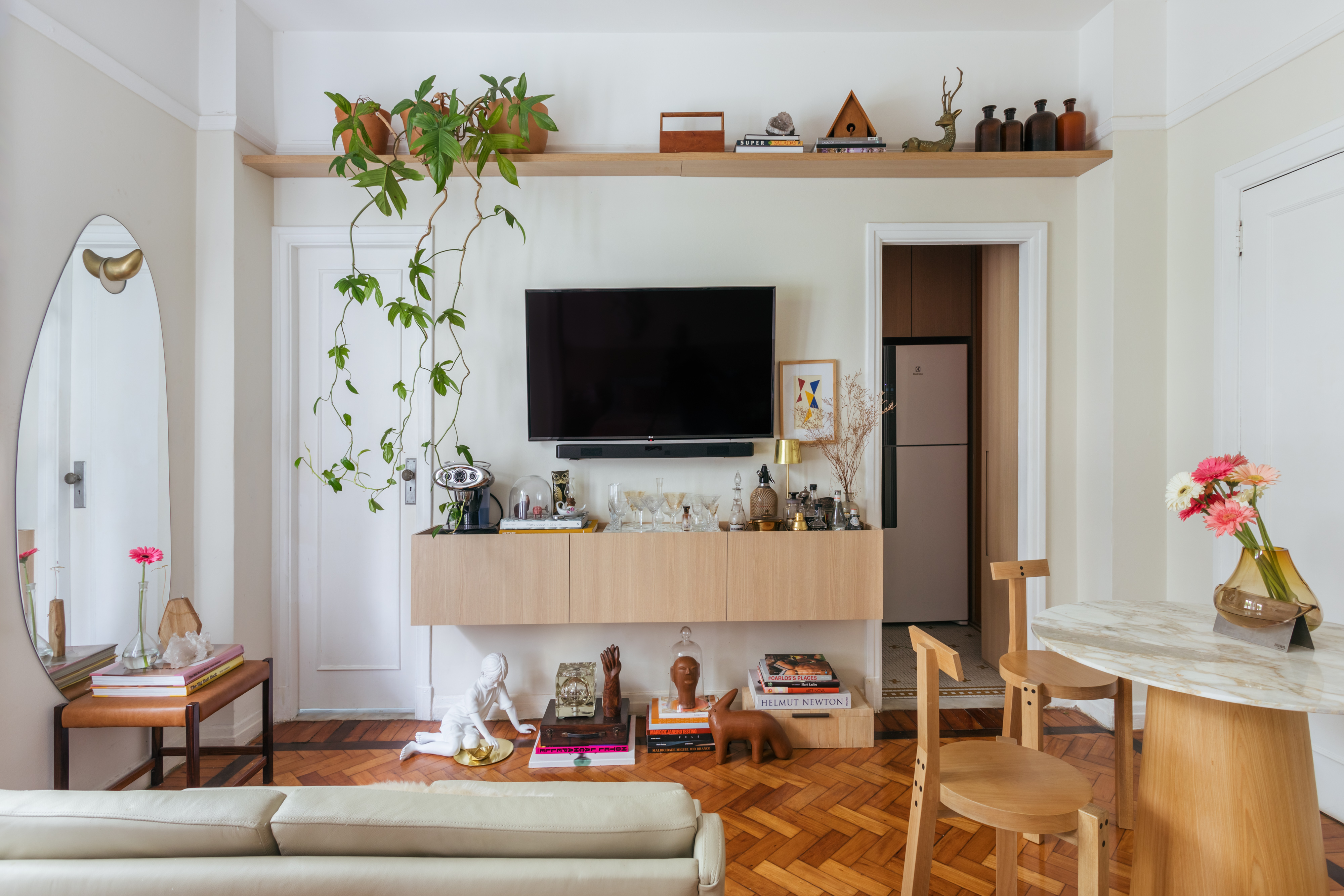 Conheça o apartamento de 42 m² do arquiteto Rodolfo Consoli em Copacabana. Na foto, sala com prateleira, tv, espelho orgânico e varanda.