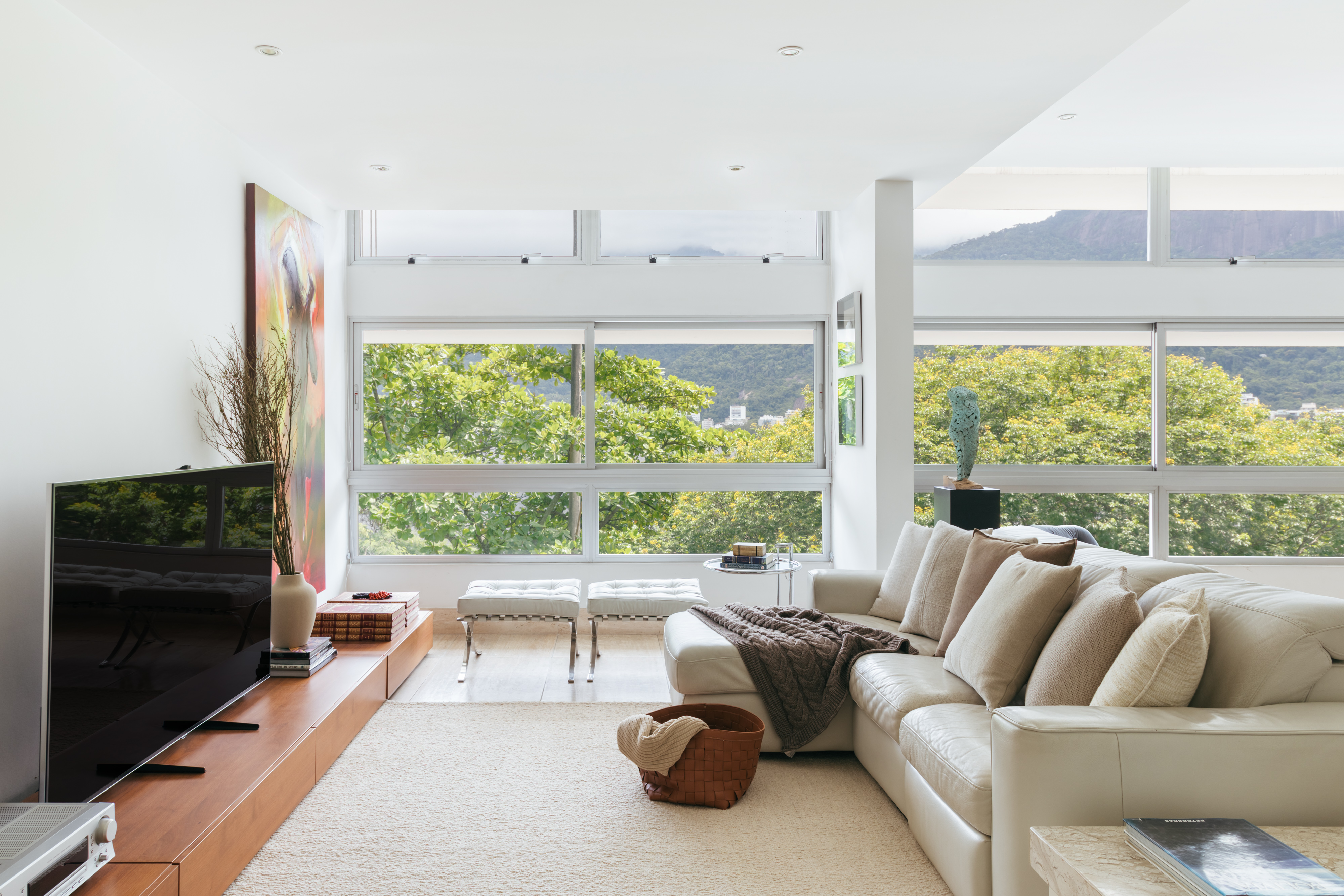 A natureza carioca circunda todo este apartamento de 245 m². Projeto de Vivian Reimers. Na foto, sala com vista para as árvores, quadros e sofás.