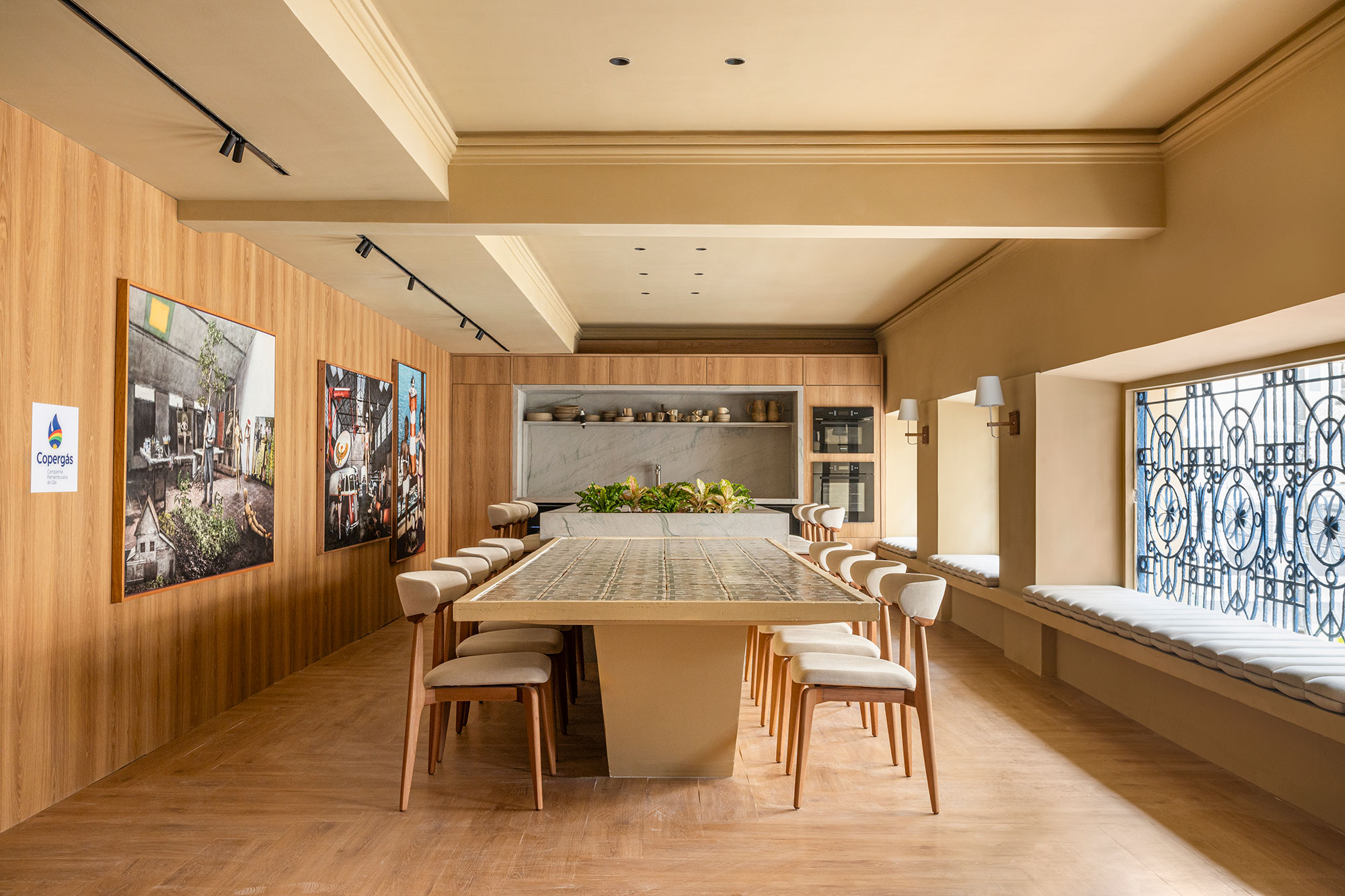 <b>Luiza Nogueira Arquitetura - Gourmet Copergás. </b>Preservando a estrutura da edificação, o projeto é um local de estar com amigos para um bom papo em torno do espaço gourmet. O gradil antigo foi preservado e um grande banco traz a área de convívio para perto das janelas. Com estrutura de gesso, a mesa ganha destaque com a cerâmica Brennand. Quadros do artista plástico João Câmara compõem o ambiente, celebrando seus 80 anos. Há também madeira e um toque de cor, que criam monocromia e aconchego.