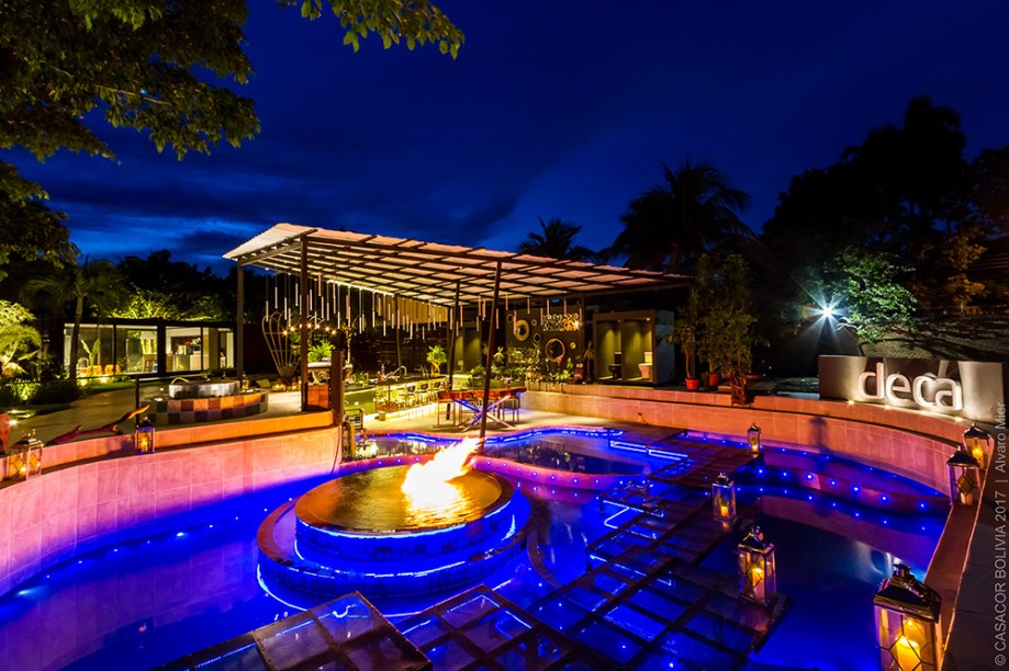 CASACOR Bolívia. Pool Bar Deca - Alejandra Iriarte. A dualidade do fogo em relação a elementos como água e ar inspira o espaço, setorizado em quatro piscinas conectadas, bar e lounge. As luzes acompanham o ritmo da música.
