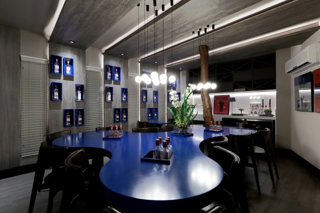 Wine & Gin Bar - Diego Ferraz. Uma grande mesa azul de linhas orgânicas envolvendo uma árvore central. O objetivo é criar um espaço elegante, porém despojado, ideal para conviver e confraternizar.