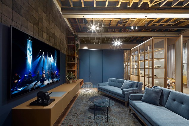 Studio Sumisura - Gislene Lopes. A parede ao fundo do ambiente o os sofás na cor azul são os destaques do ambiente, integrado por painéis pivotantes de vidro que integram os ambientes sem roubar a cena