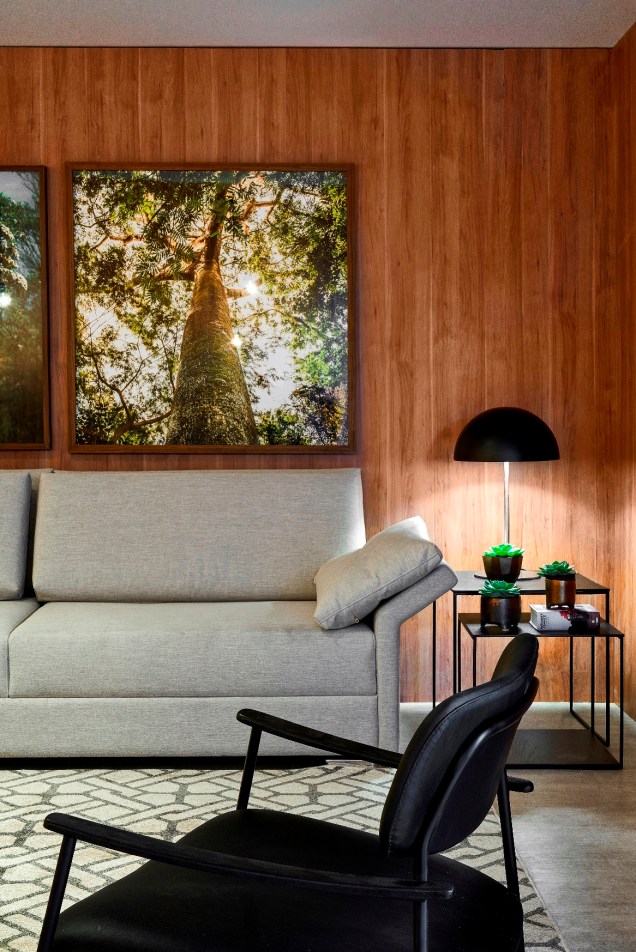 Lounge Resort - Gui Rodrigues. Nesse ambiente, as árvores estão presentes em fotografias as quais, junto de plantas, preenchem a estante que divide o ambiente.