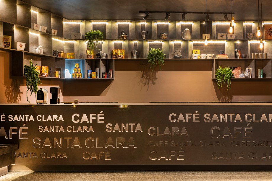 Café Santa Clara - Mesquita & Belém Arquitetura e Design. A iluminação é um recurso central na criação do espaço. Ela está presente nos nichos com aparência de concreto, que destacam utensílios e produtos, além de valorizar a marca vazada no balcão. Na cartela de cores, cores naturais remetem aos grãos de café.