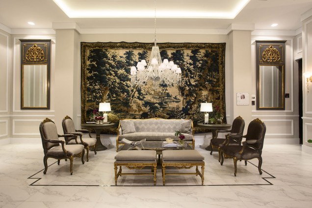 Bien Venue - Milena Niemeyer. Boas-vindas no melhor estilo clássico marcam o foyer de entrada. Uma grande sala de estar, majoritariamente branca, cria um ambiente sofisticado e elegante, destacando as peças de mobiliário e decoração.