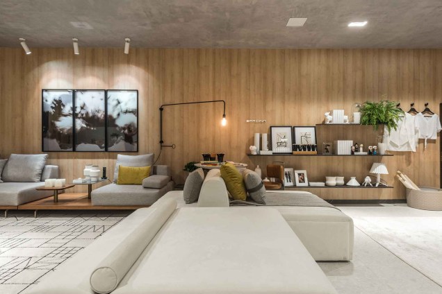 O amadeirado aparece no loft como a textura favorita, aparecendo como revestimento da maior parede do ambiente. Um grande sofá modular divide o quarto com a prateleira suspensa, que confere geometria à decoração.