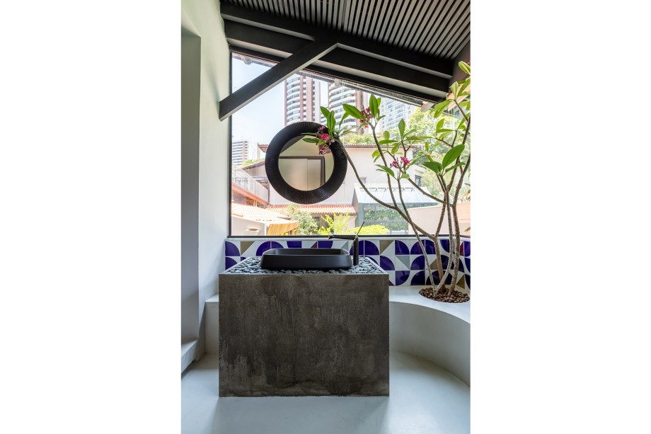 O banheiro emoldura um belo jardim que ganha vida ao fundo. Nele, o concreto é usado para dar suporte à cuba. O destaque aqui, porém, fica para os ladrilhos hidráulicos azuis, que também fazem referência ao modernismo brasileiro e à nomes como Athos Bulcão.