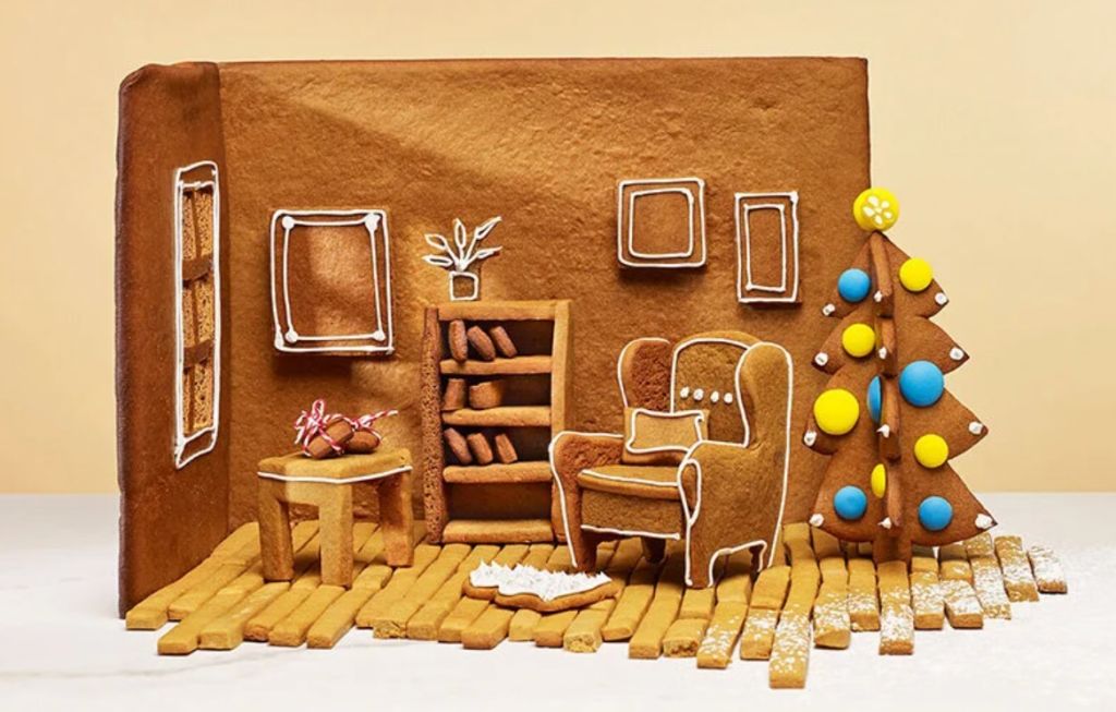 Canto de uma casinha de biscoito com poltrona, estante, mesa de apoio e árvore de Natal, todos feitos de biscoito