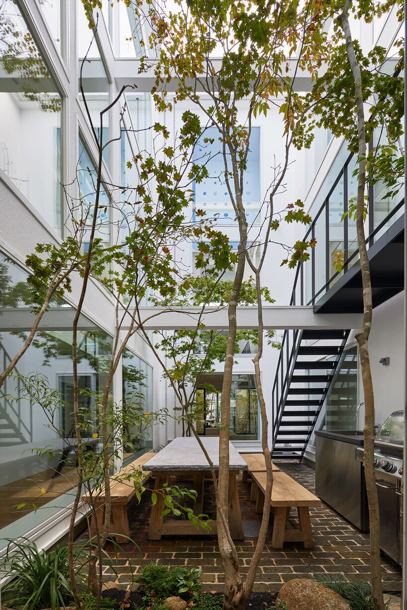 pátio do projeto minimalista com vegetação e árvore no centro. Mesa de convívio para a família e churrasqueira também se encontram no local