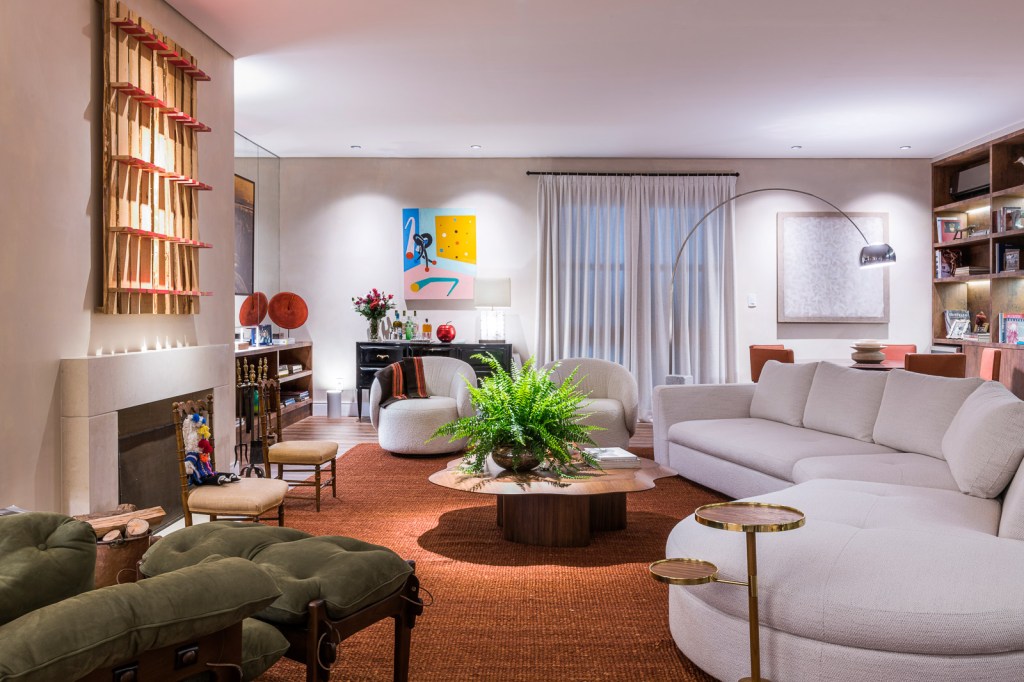 Sala de estar com tapete laranja; mesa de centro; espaço para lareira e sofá curvo branco