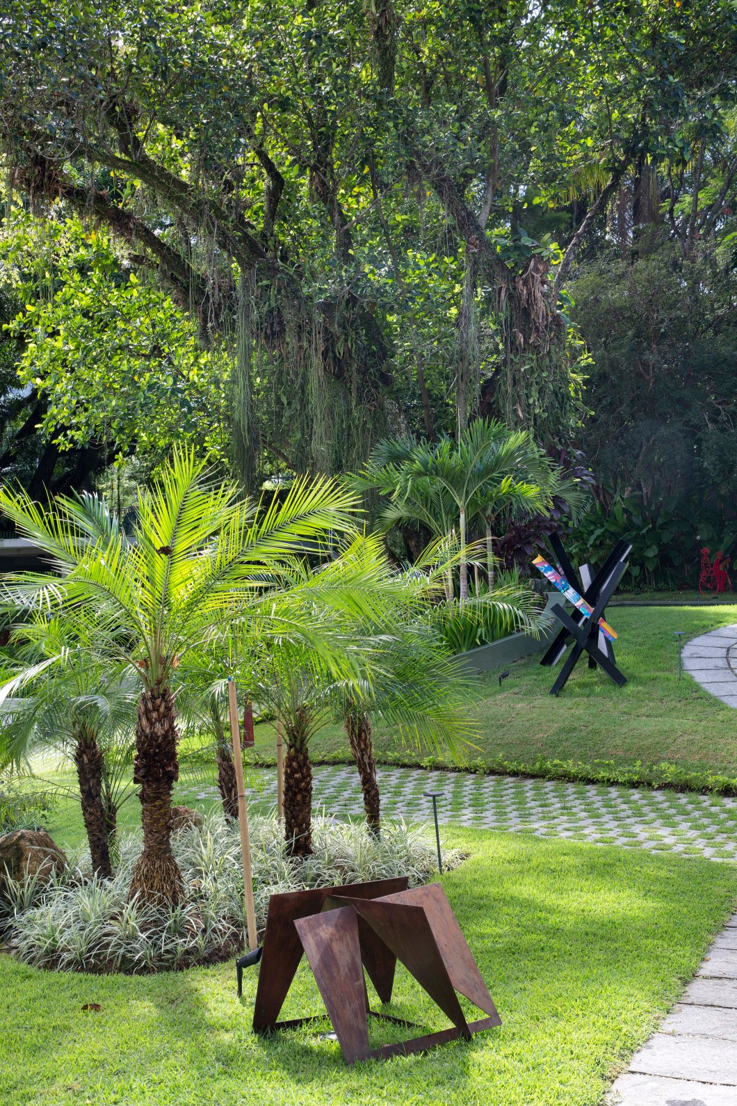 No primeiro plano, palmeiras-fênix (Phoenix roebelenii), em diversos tamanhos, e liríope variegata (Liriope spicata) como forração. Obra de arte: escultura de Bob Cardim.