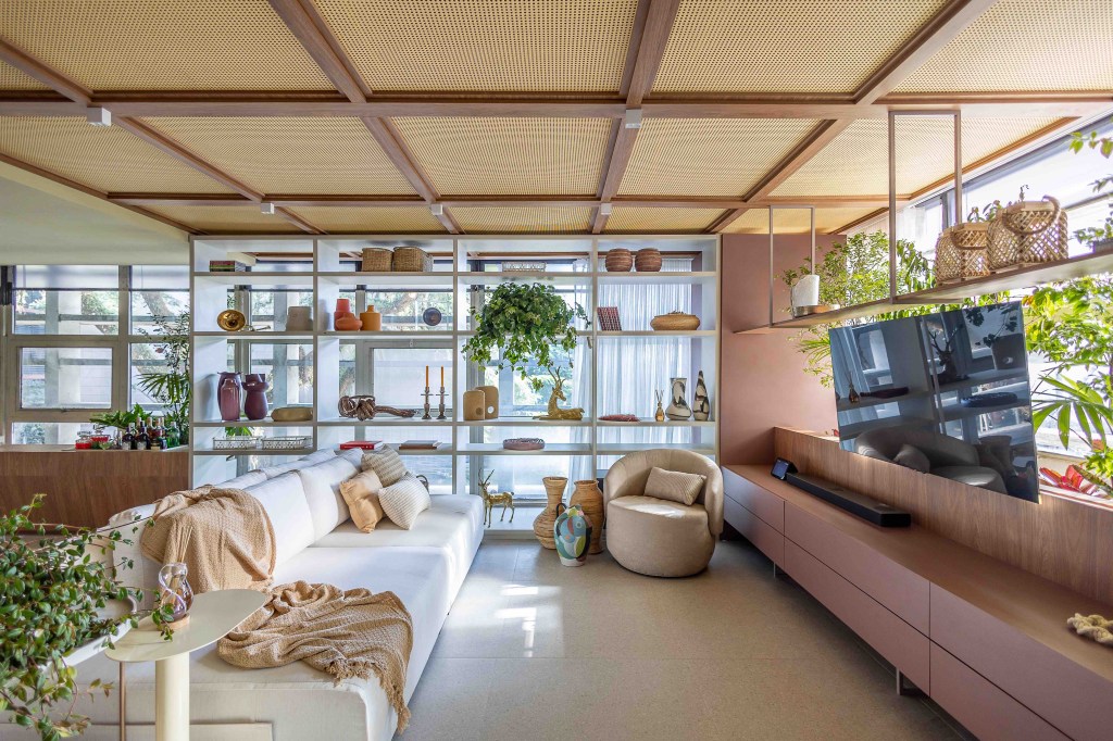 ARQTAB | Maycon Fogliene - A Casa do Ser. Projeto da CASACOR São Paulo 2023. Na foto, sala integrada com a cozinha, estante, poltrona, sofá e TV.