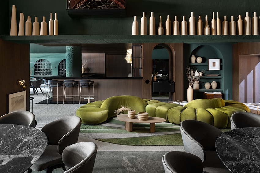 Altera Arquitetura - Ninho & Aspargos. Projeto da CASACOR São Paulo 2023. Na foto, restaurante com sofá curvo verde, paredes de madeira e cores escuras.