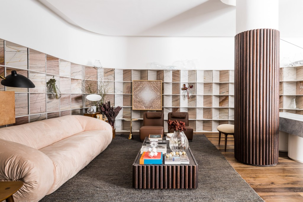 Marcela Penteado Arquitetos - Loft 011. Projeto da CASACOR São Paulo 2023. Na foto, sala de estar com estante curva, tapete e sofa..
