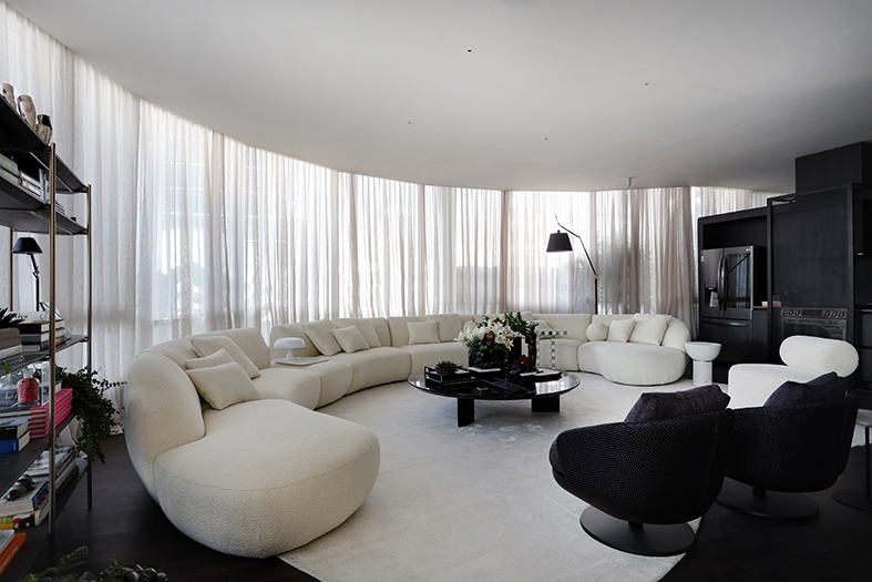 Moacir Schmitt Jr. e Salvio Moraes Jr. - O primeiro loft. Projeto da CASACOR São Paulo 2023. Na foto, sala de estar com sofá curvo branco, tapete, estante e poltronas.