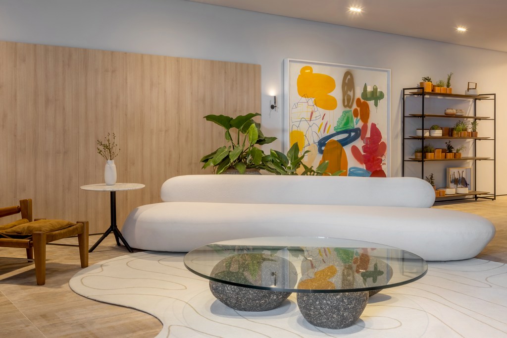 Natiara Reis e Paulo Reis - Loft Um. Projeto da CASACOR Goiás 2023. Na foto, sala de estar com sofá curvo branco e parede de madeira.