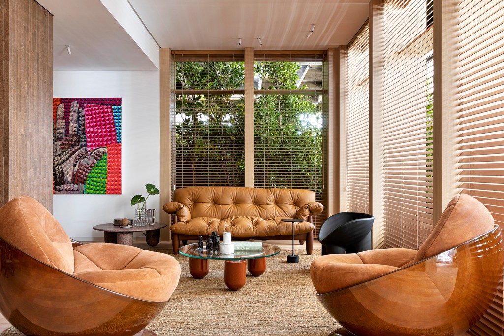 Tufi Mousse Arquitetura - A Casa Morena. Projeto da CASACOR São Paulo 2023. Na foto, sala com sofa de couro, persianas e tapete.