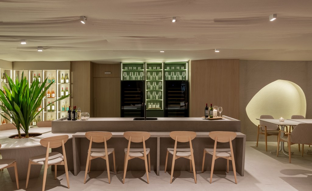 Vilaville Arquitetura - Restaurante Horta. Projeto da CASACOR São Paulo 2023. Na foto, mesa redonda com plantas, balcão de bar e adega iluminada.