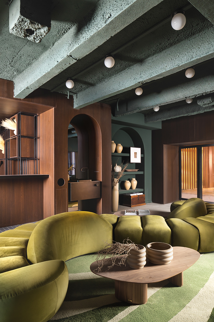 Altera Arquitetura - Ninho & Aspargos. Projeto da CASACOR São Paulo 2023. Na foto, restaurante com sofá curvo verde, paredes de madeira e cores escuras.
