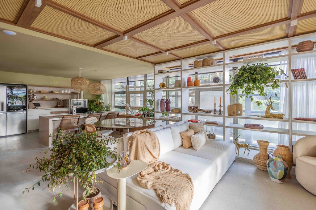ARQTAB | Maycon Fogliene - A Casa do Ser. Projeto da CASACOR São Paulo 2023. Na foto, sala integrada com a cozinha e jantar. Sofá branco, estante e teto de fibra.