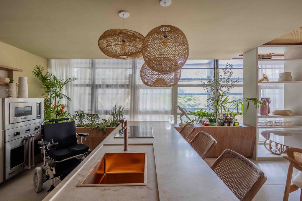 ARQTAB | Maycon Fogliene - A Casa do Ser. Projeto da CASACOR São Paulo 2023. Na foto, cozinha com bancada integrada ao estar com luminaria de fibra e mesa de jantar de vidro.