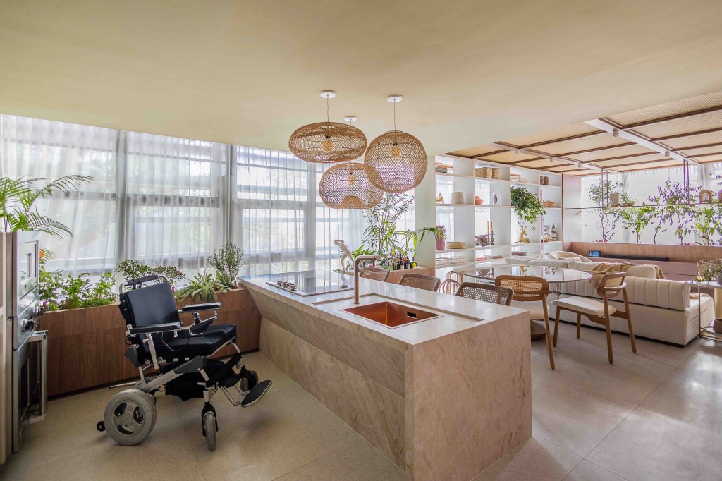 ARQTAB | Maycon Fogliene - A Casa do Ser. Projeto da CASACOR São Paulo 2023. Na foto, sala de jantar integrada ao estar com estante, mesa redonda e bar. Cozinha acessível com bancada.