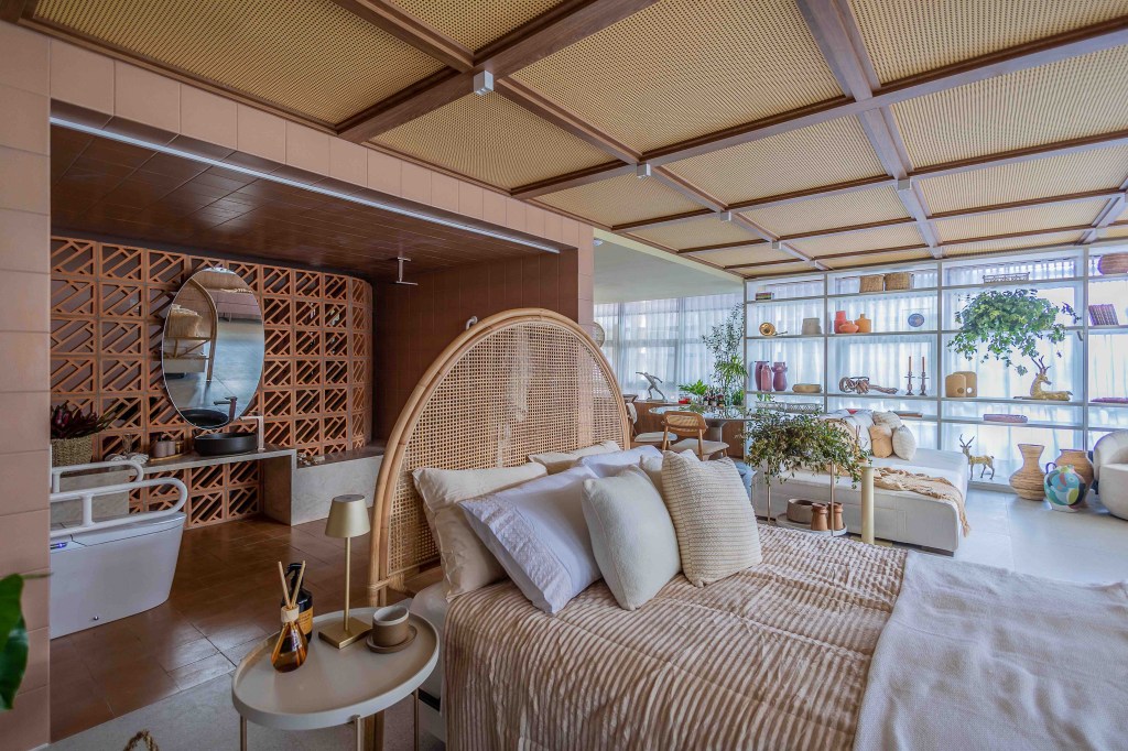 ARQTAB | Maycon Fogliene - A Casa do Ser. Projeto da CASACOR São Paulo 2023. Na foto, quarto de casal com cama com cabeceira de palhinha. banheiro integrado com parede de cobogós.