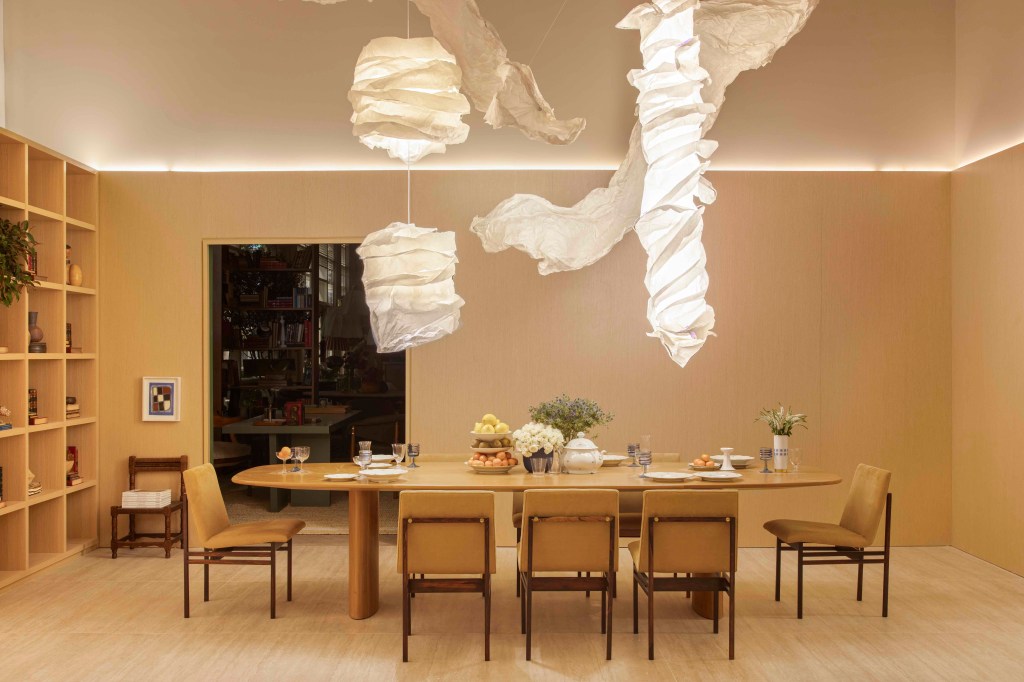 Da Hora Arquitetura - Loft Vastu. Projeto da CASACOR São Paulo 2023. Na foto, sala de jantar com luminária orgânica, estante de madeira e pé-direito duplo.