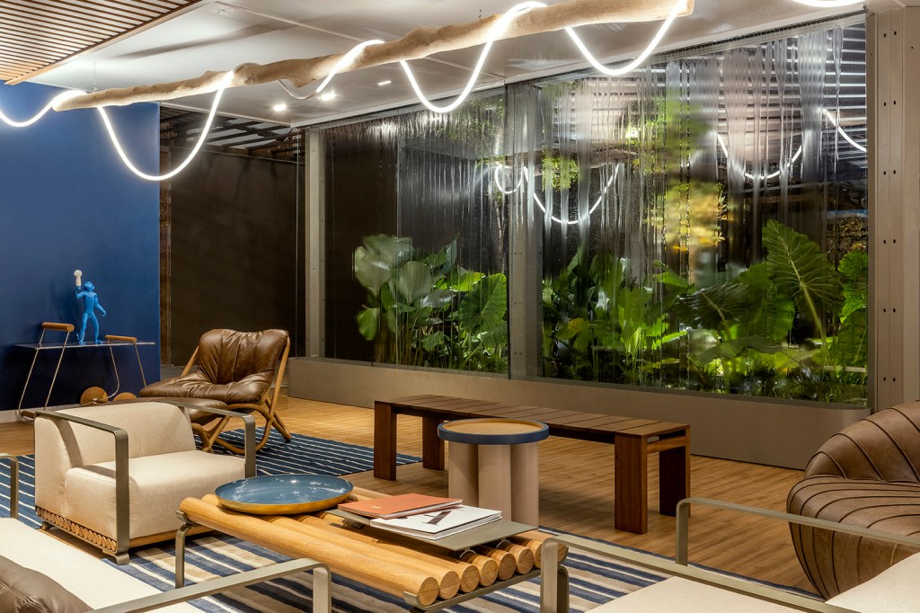 Diego Mendonça e Heloá Vaz - Lounge BRB. Projeto da CASACOR Goiás 2023. Na foto, lounge com vista para o jardim, parede azul e luminária de corda.
