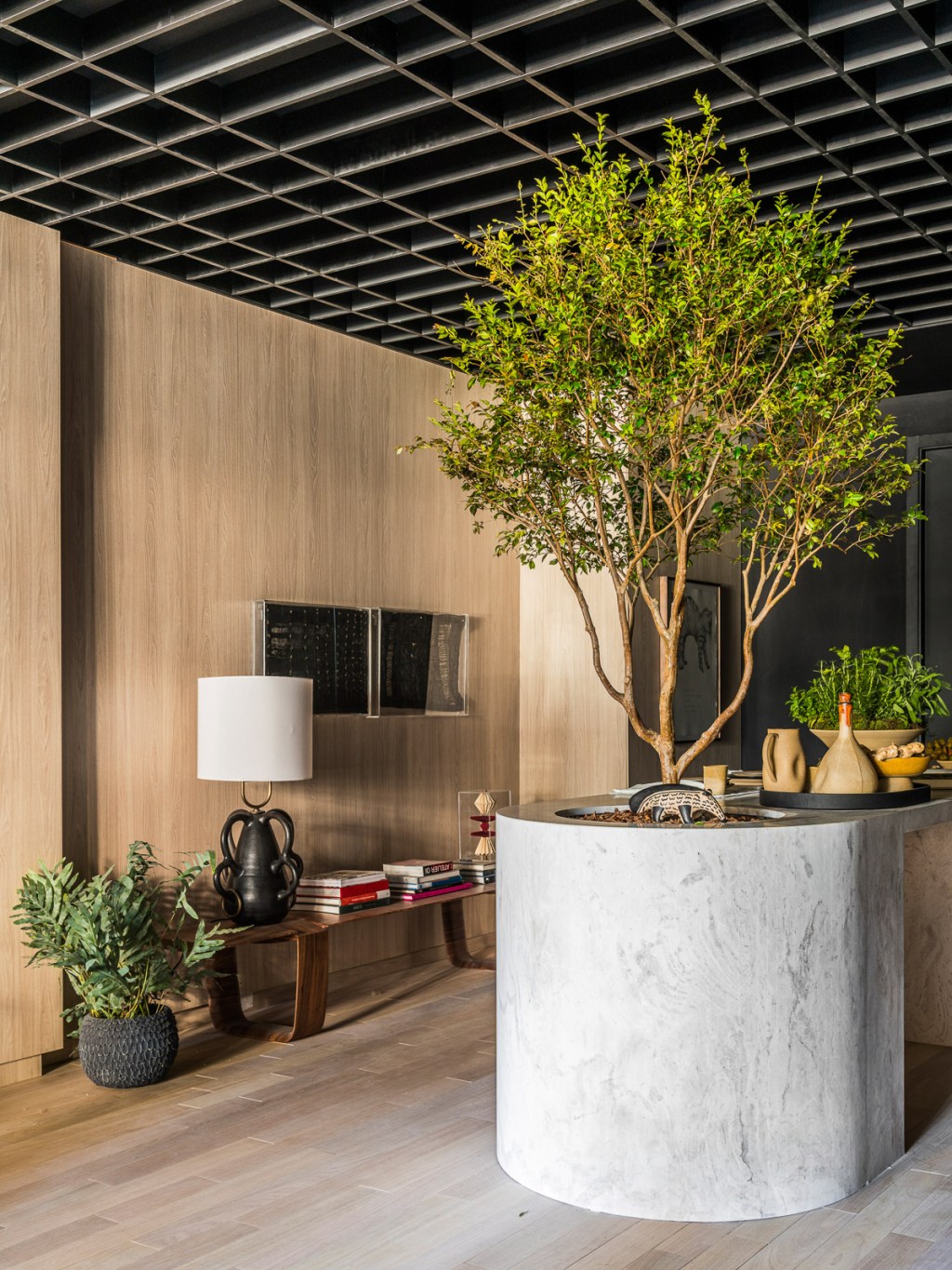 Érica Salguero Arquitetura - Espaço Solitude. Projeto da CASACOR São Paulo 2023. Na foto, sala com parede de madeira e quadros. Bancada com árvore.