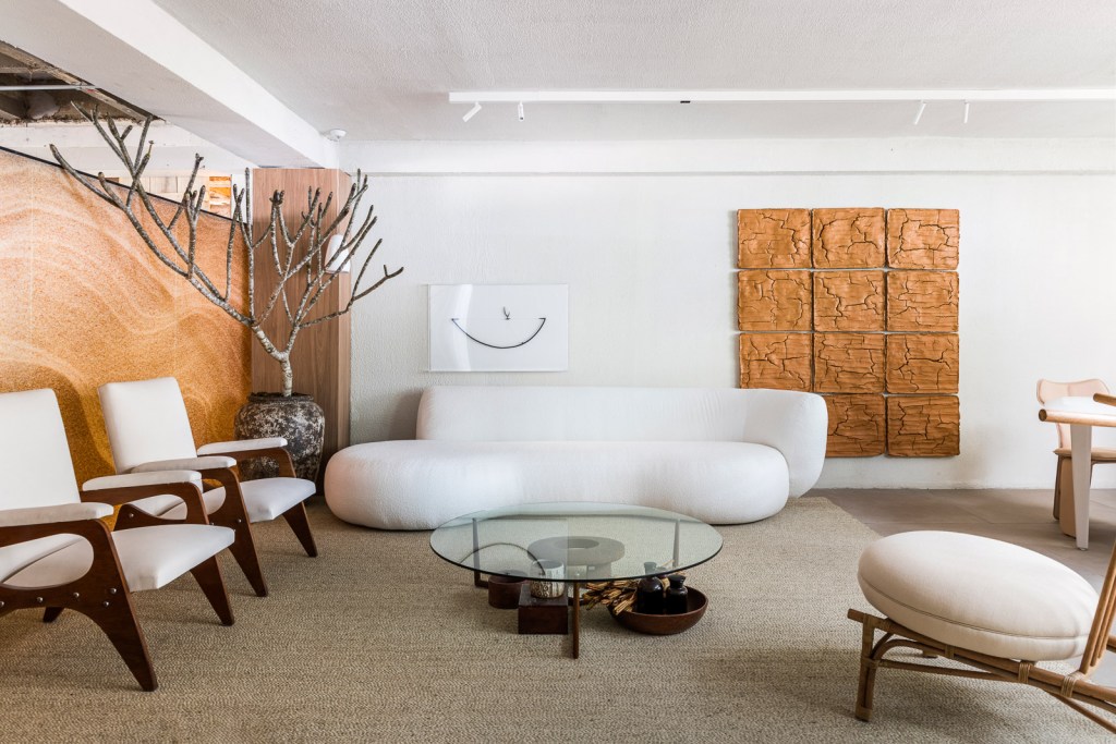 Gustavo Martins Arquitetos - Odoiá. Projeto da CASACOR São Paulo 2023. Na foto, sala de estar com sofa curvo, tapete e quadro feito de lama.