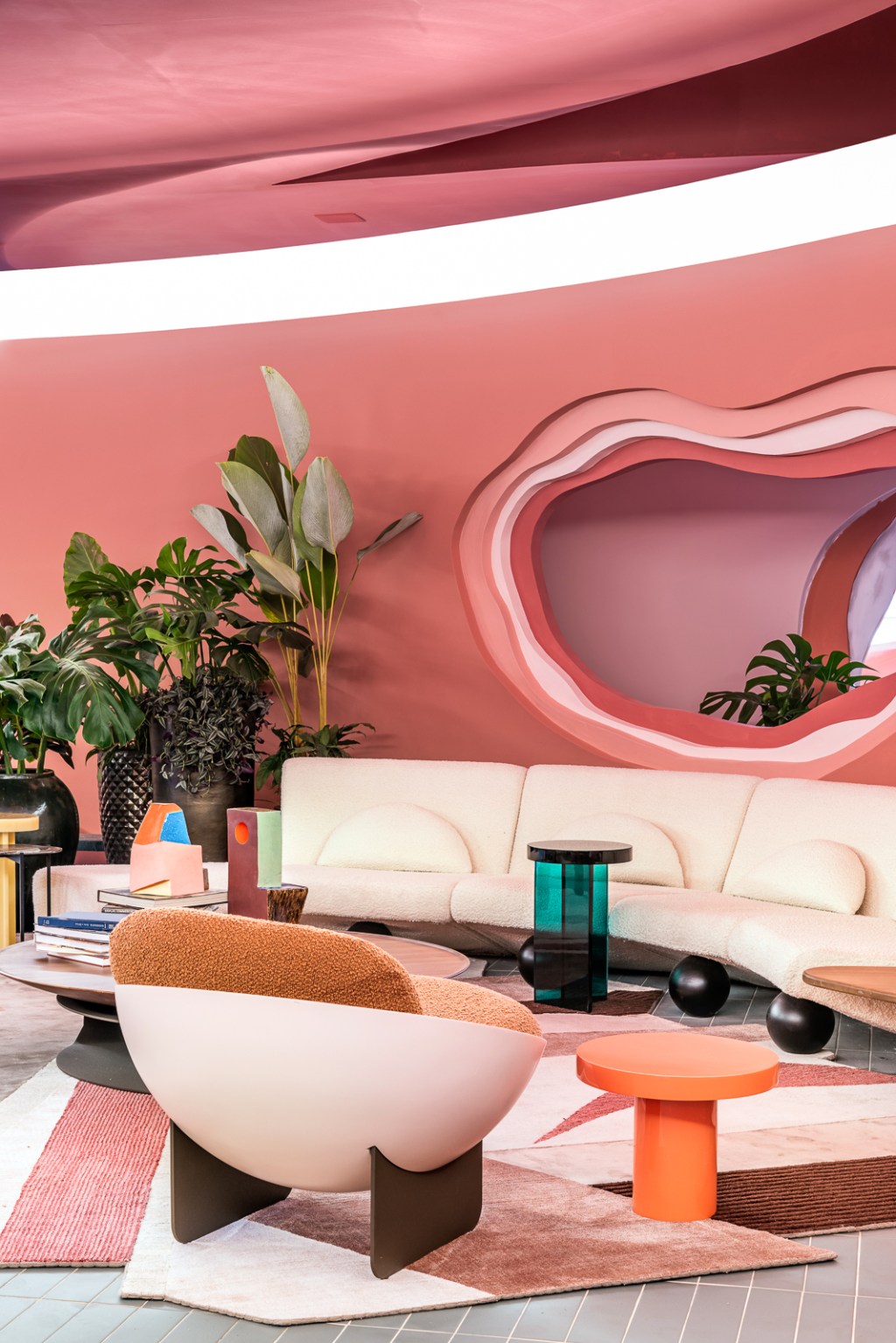 Ricardo Abreu - Casa Coral. Projeto da CASACOR São Paulo 2023. Sala com paredes rosas, sofá curvo, plantas e tapete.