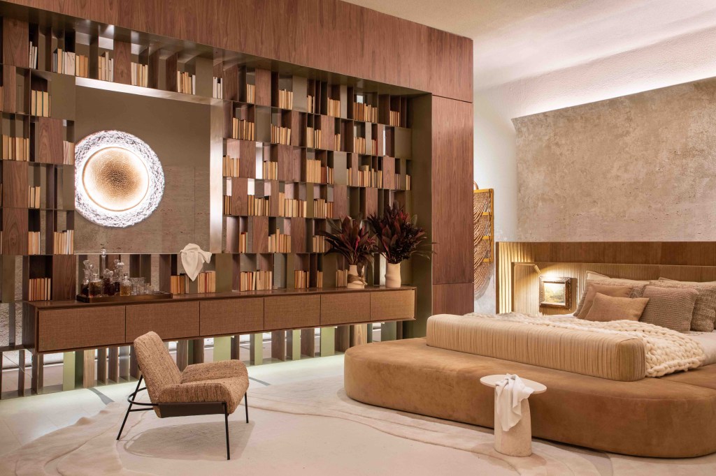 Suite Arquitetos - Casa Kraftizen Cosentino. Projeto da CASACOR São Paulo 2023. Na foto, quarto com cama estofada, estante com livros e paredes de madeira.