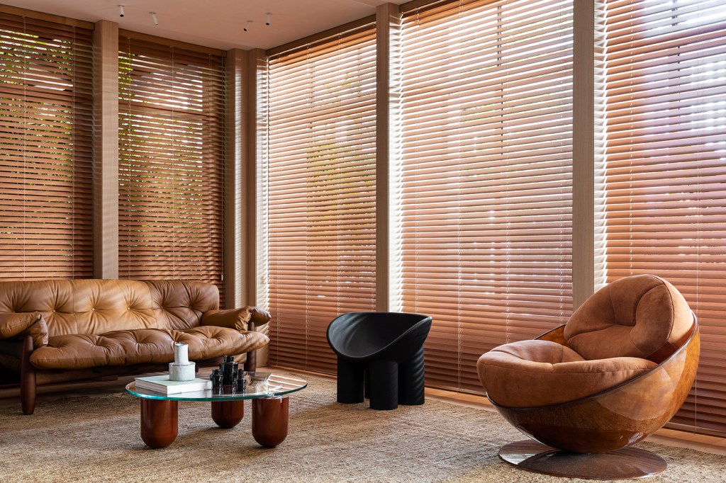 Tufi Mousse Arquitetura - A Casa Morena. Projeto da CASACOR São Paulo 2023. Na foto, sala de estar com sofá de couro, persianas e tapetes.