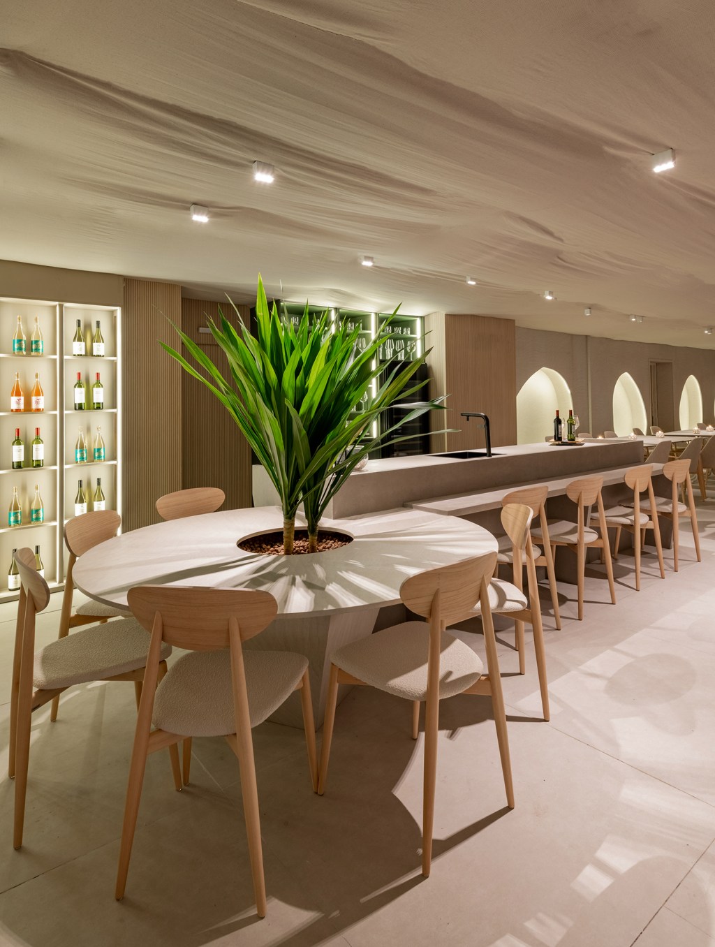 Vilaville Arquitetura - Restaurante Horta. Projeto da CASACOR São Paulo 2023. Na foto, mesa redonda com plantas, balcão de bar e adega iluminada.