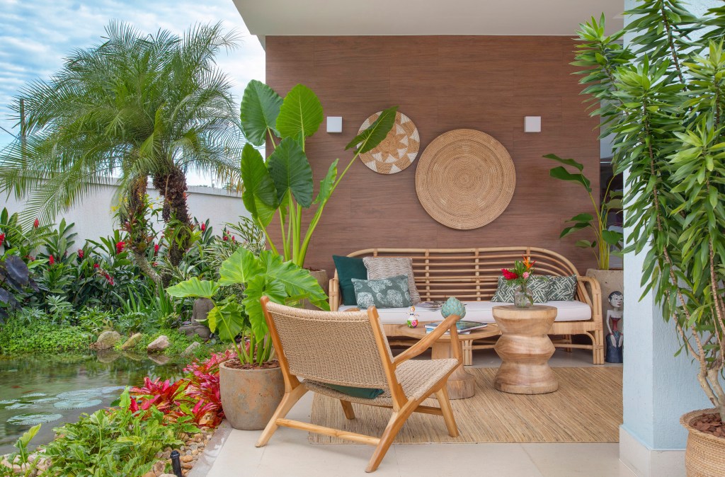 Jardim de 900 m² tem lago com peixes, praia de areia branca e pomar. Projeto de Ana Veras e Bernardo Vieira. Na foto, varanda com sofá, lago e vasos com plantas.