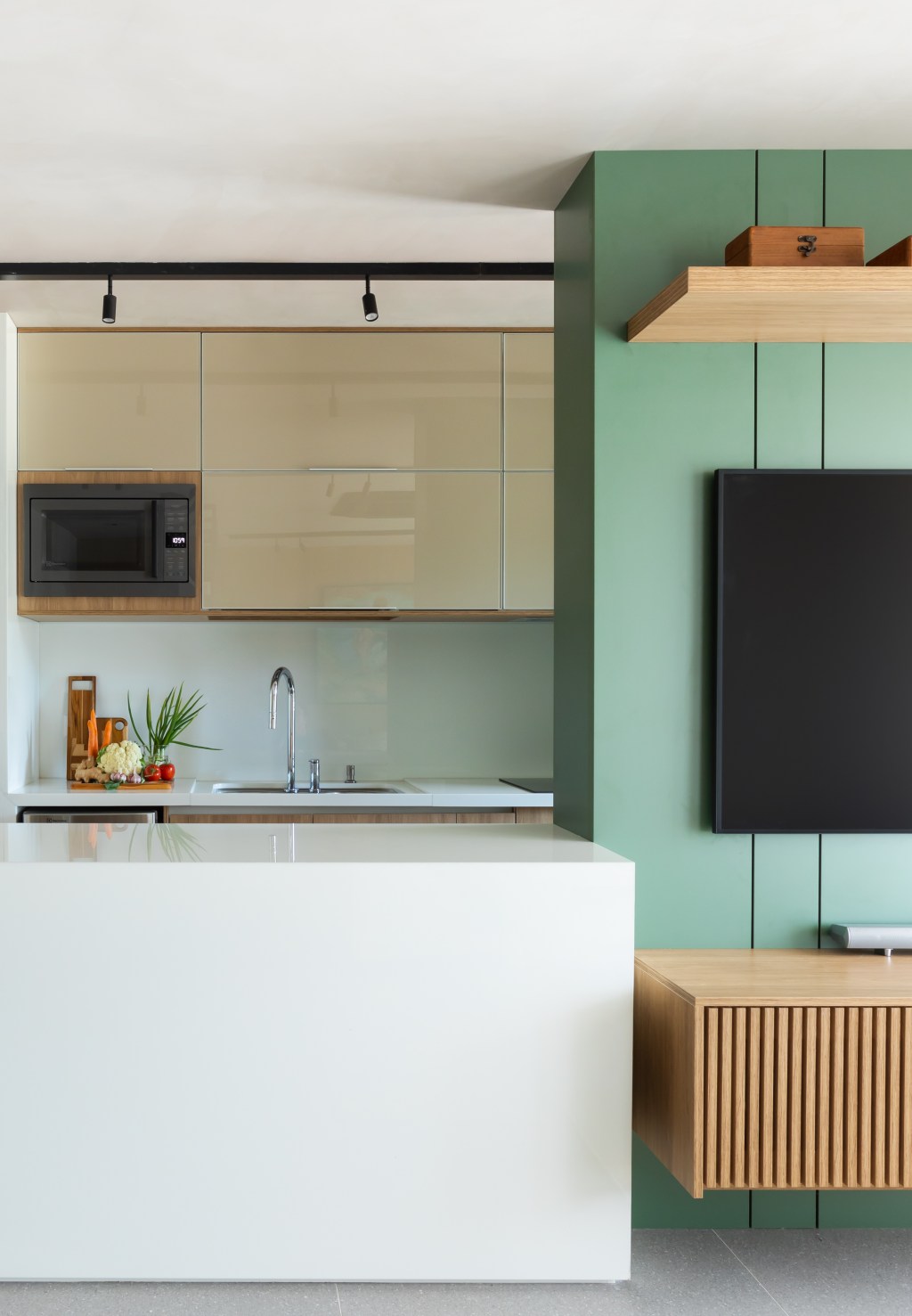 Apê de 82 m² ganha décor japandi com toques contemporâneos. Projeto de Fabiano Ravaglia. Na foto, sala integrada com a cozinha com balcão branco. Parede verde com TV.