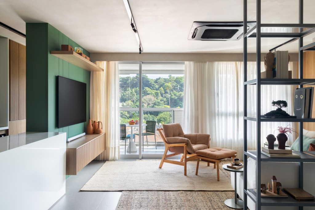 Apê de 82 m² ganha décor japandi com toques contemporâneos. Projeto de Fabiano Ravaglia. Na foto, sala de estar com parede verde, tv e varanda.